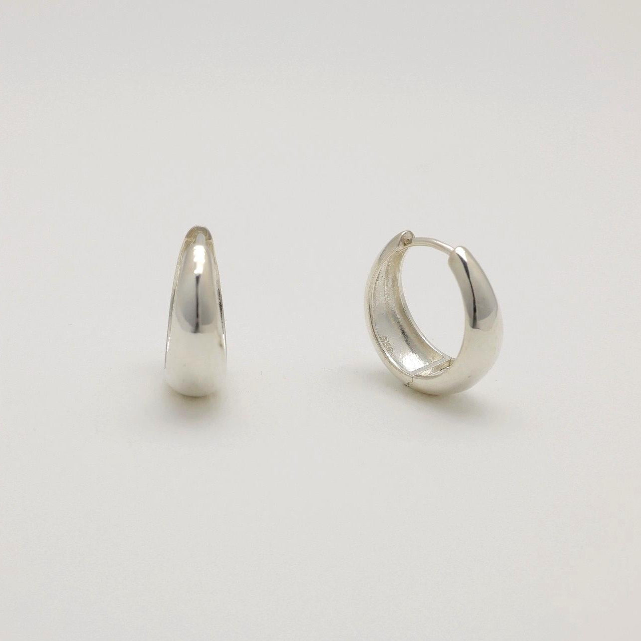 Two silver hoop earrings on a light gray background