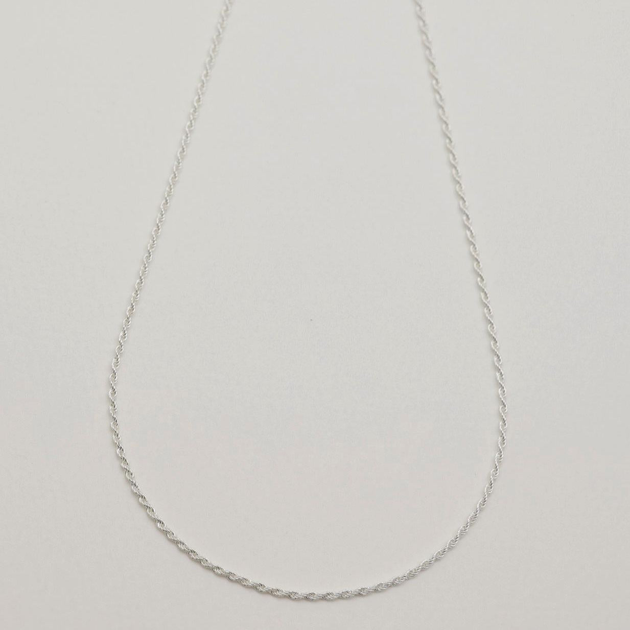 A sterling silver rope chain necklace with fine twisted links, displayed on a light neutral background. 42cm length, polished finish