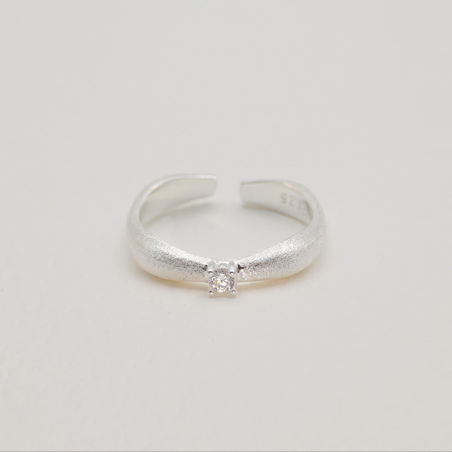 Hero image of curved silver ring on neutral background