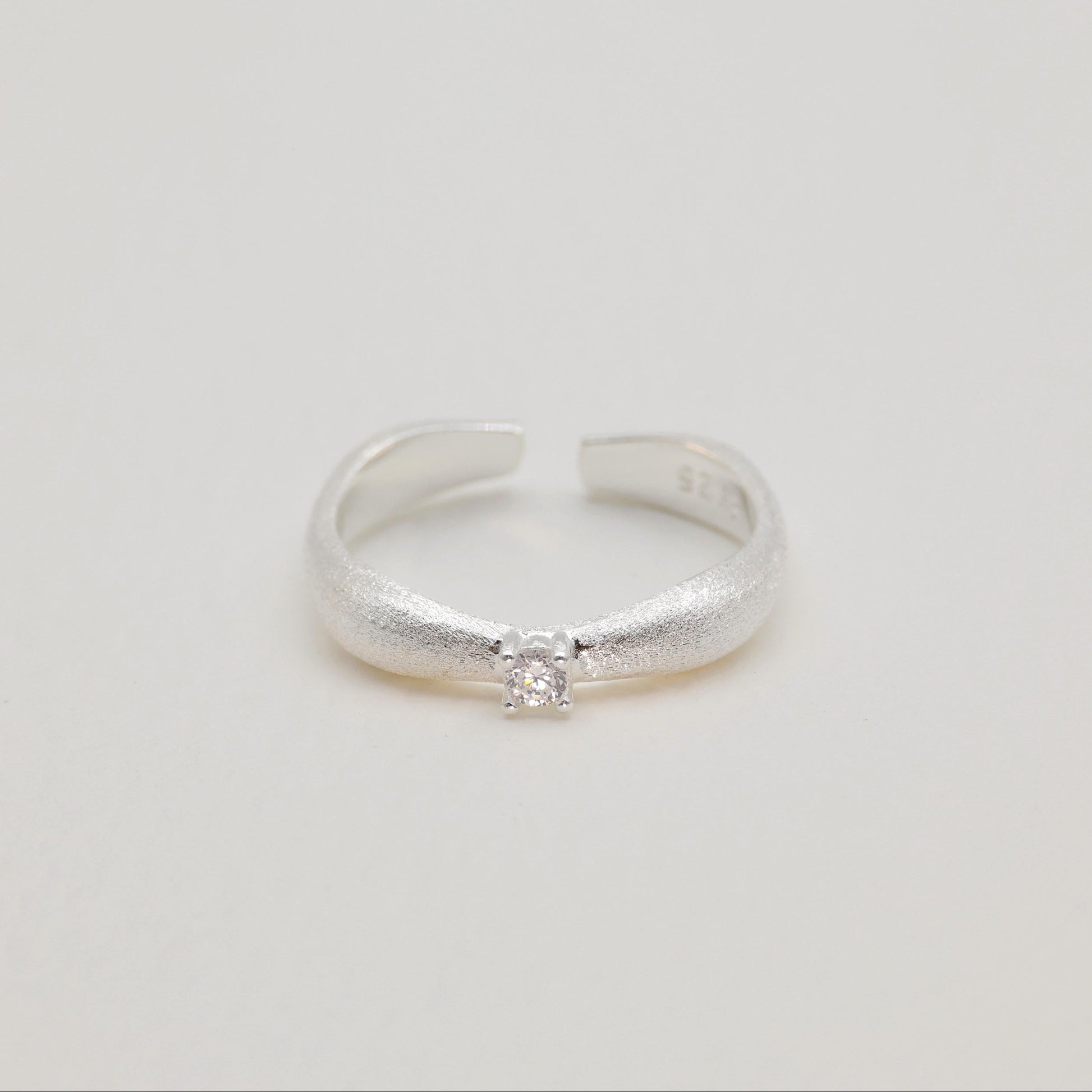 Hero image of curved silver ring on neutral background