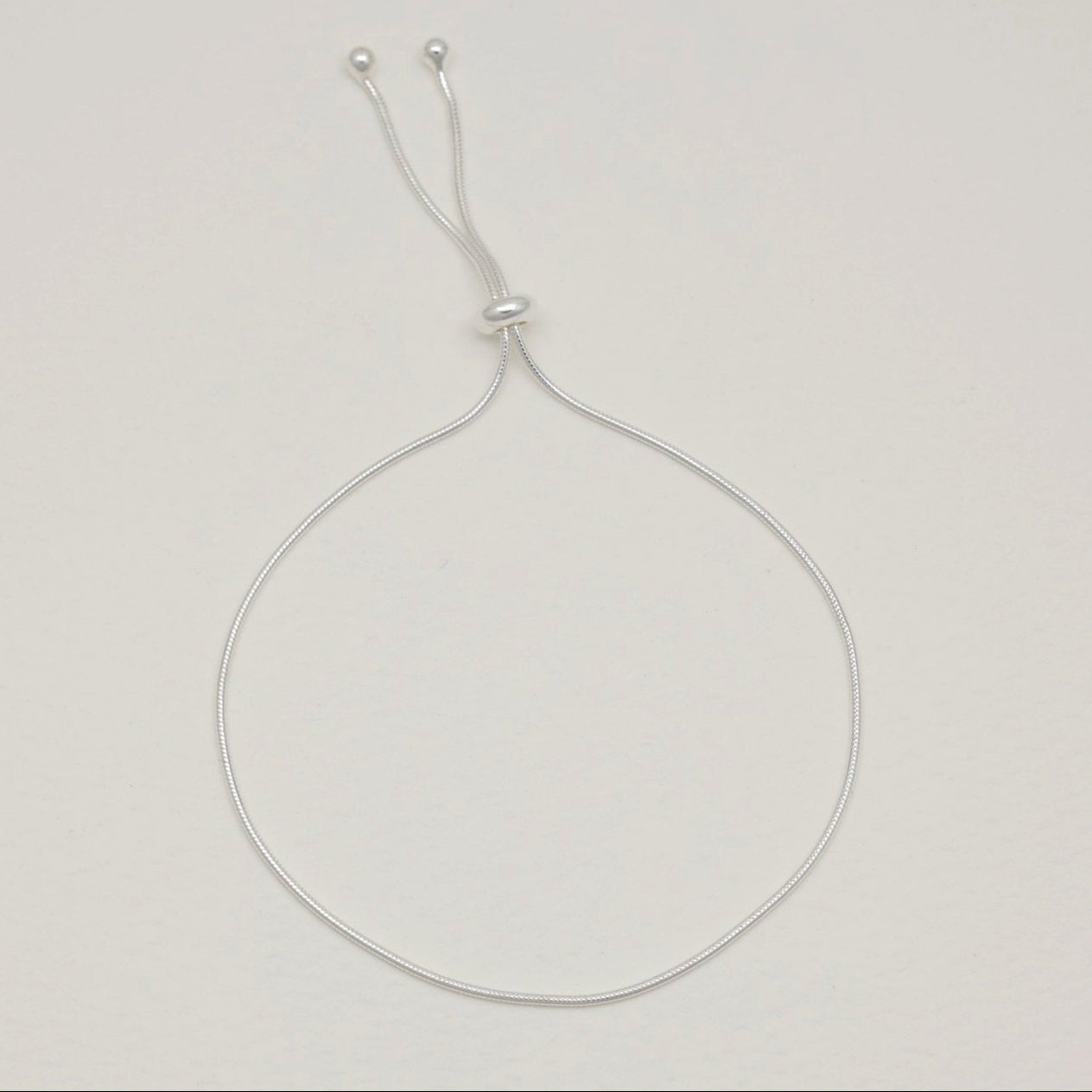 Sterling silver adjustable bracelet with sliding bead, styled in a rounded open loop on a soft-toned background.