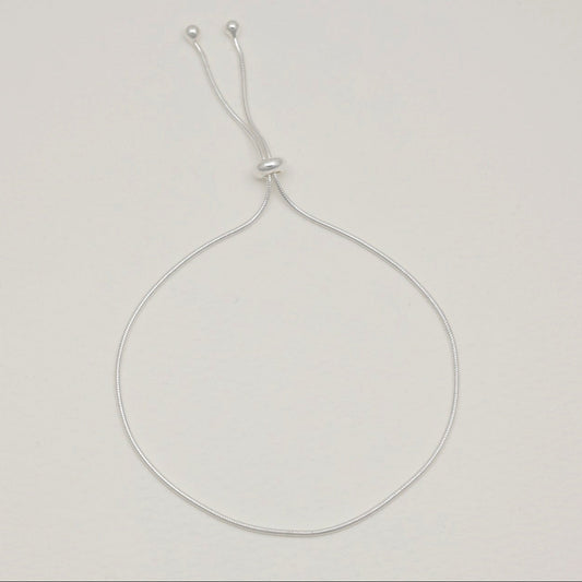 Sterling silver adjustable bracelet with sliding bead, styled in a rounded open loop on a soft-toned background.