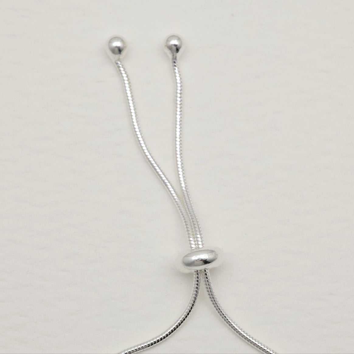 Sterling silver adjustable bracelet with sliding bead, styled in a rounded open loop on a soft-toned background.