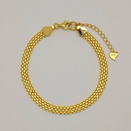 Gold vermeil mesh bracelet arranged in a full circle on a neutral background, showcasing its polished woven texture and lobster clasp with heart tag extender.
