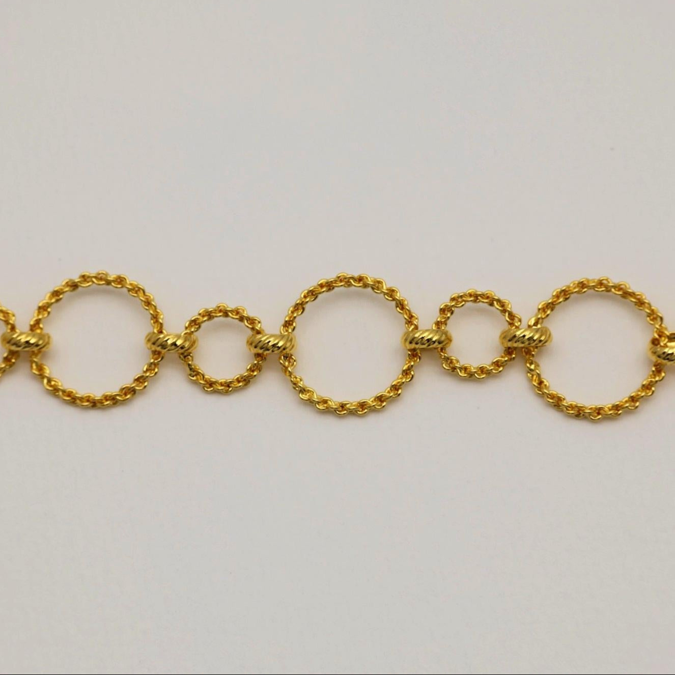 Close-up of twisted gold vermeil circle links in varying sizes, laid flat on neutral background