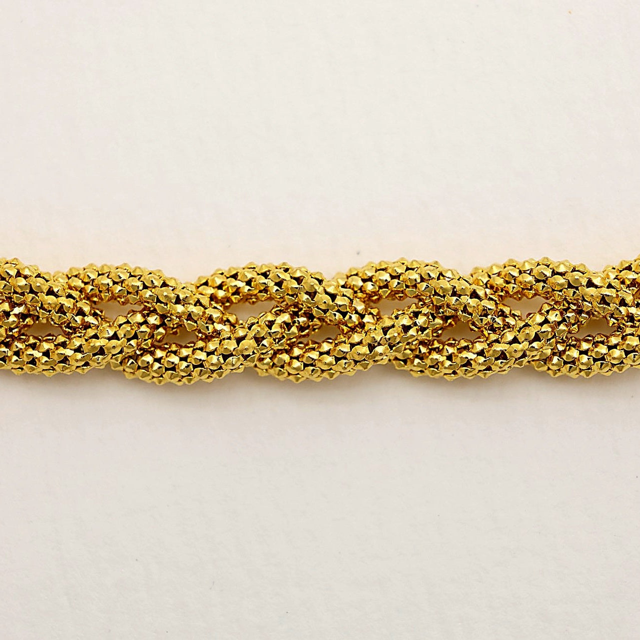 Close-up of Béatrice Twist Bracelet’s faceted gold vermeil links on white background.