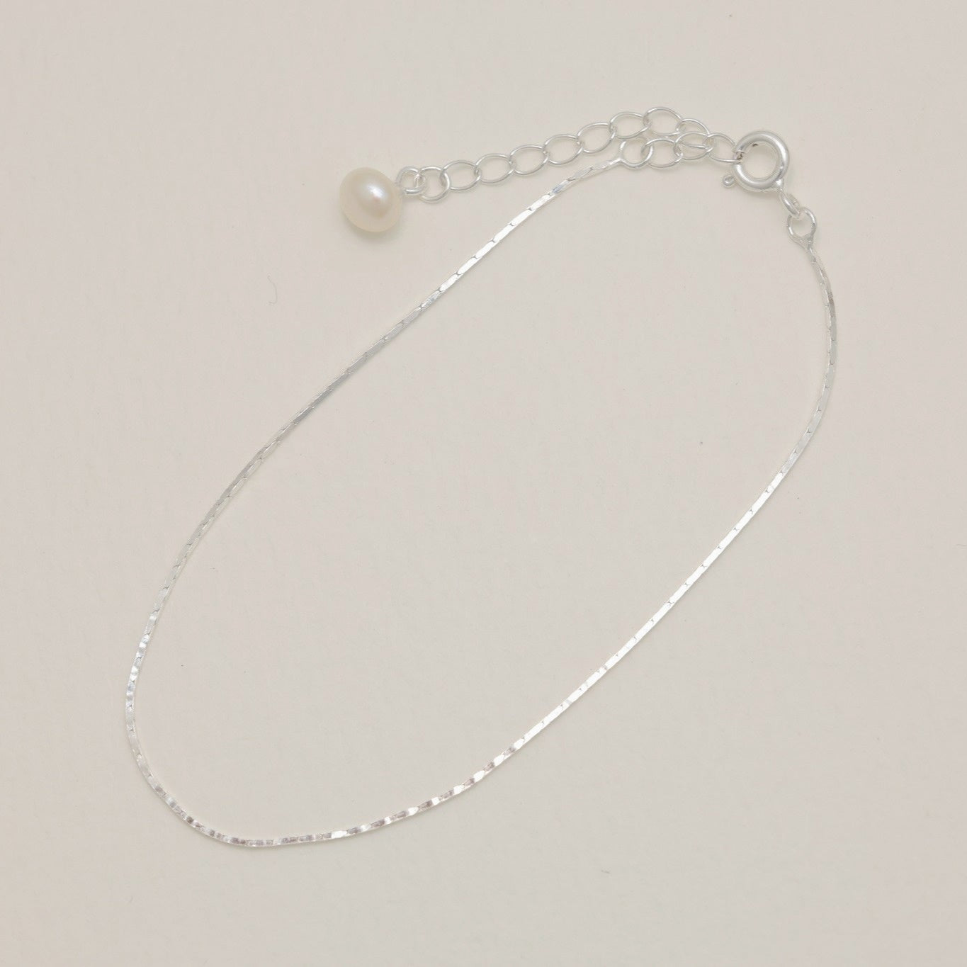 “Top view of delicate silver chain bracelet with pearl drop”

