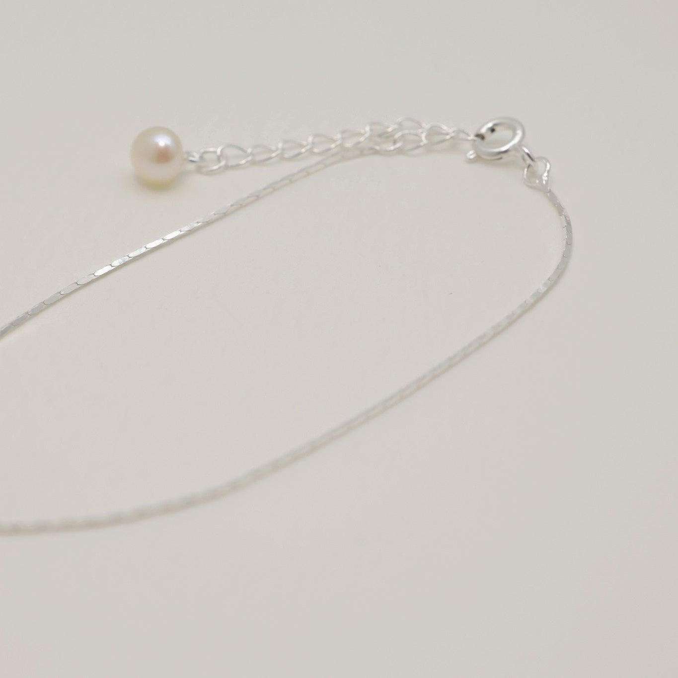 “Thin polished sterling silver bracelet with single pearl charm on white background”

