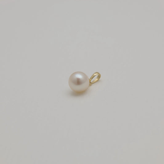Minimalist gold and pearl pendant photographed from distance on cream backdrop