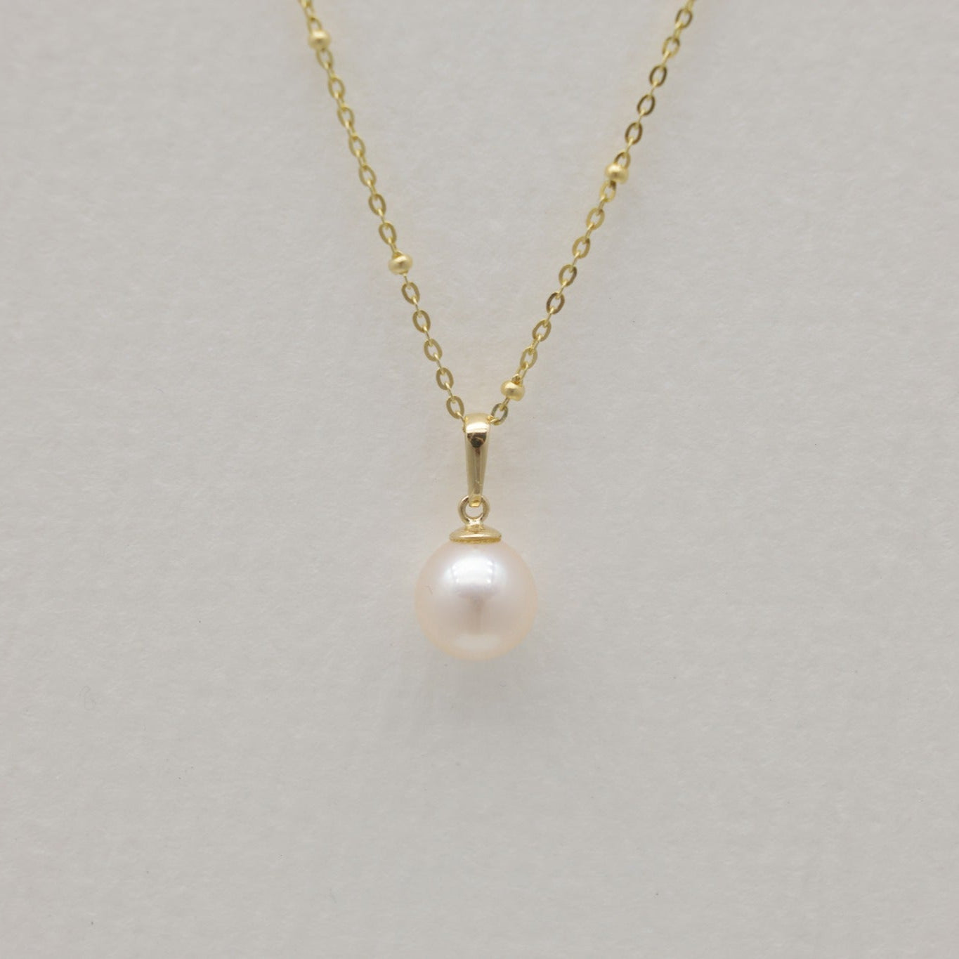 Natural pearl necklace on chain with 14K gold bail against white background